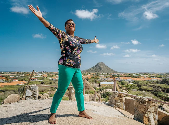 Sharon Burgler met open armen in Arubaanse natuur. Beeld van vrijheid, veerkracht en de oorsprong van Manitu’s werkwijze.
